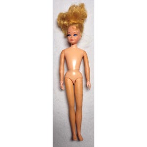 May include: A vintage doll with a nude body and blonde hair styled in an updo. The doll has blue eyes and is standing upright. The doll's skin tone is a light peach colour.