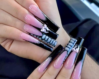 May include: Long, pink and black stiletto nails with a white bow design. The nails are very long and have a sharp point.