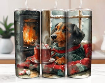 Könnte beinhalten: Ein Set aus drei Edelstahl-Bechern mit einem winterlichen Weihnachtsmotiv. Die Becher zeigen einen Dackel, der einen Pullover trägt und an einem Kamin mit einer Tasse heißer Schokolade sitzt. Die Becher sind mit einem rot-grünen Karomuster verziert.