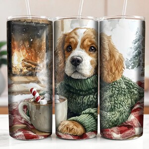 May include: A white ceramic tumbler with a green and brown dog wearing a green sweater and a red and white plaid blanket. The dog is holding a mug of hot chocolate with marshmallows and a candy cane.