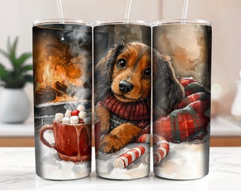 May include: A white tumbler with a red and green plaid design. A brown and white dog with a red sweater is curled up in the plaid. The dog is looking at the viewer. The tumbler has a straw and a red mug with marshmallows and hot chocolate in front of the dog.