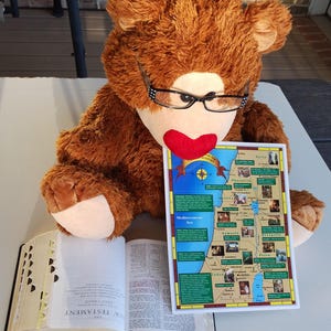 May include: A brown teddy bear wearing glasses is holding a map of the Holy Land. The map shows the location of different cities and regions, including Jerusalem, Galilee, and Samaria. The map is labeled "The Holy Land Ministry".