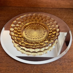 May include: A small, amber-colored glass dish with a raised, textured pattern. The dish is sitting on a silver-colored mirrored surface.