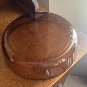 May include: A clear glass dome with a brown tint. The dome is sitting on a wooden surface.