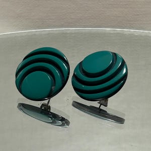 May include: A pair of green clip-on earrings with a circular design featuring concentric circles.