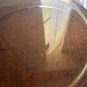 May include: A clear glass pie plate with a slightly rippled surface. The plate is sitting on a wooden surface.