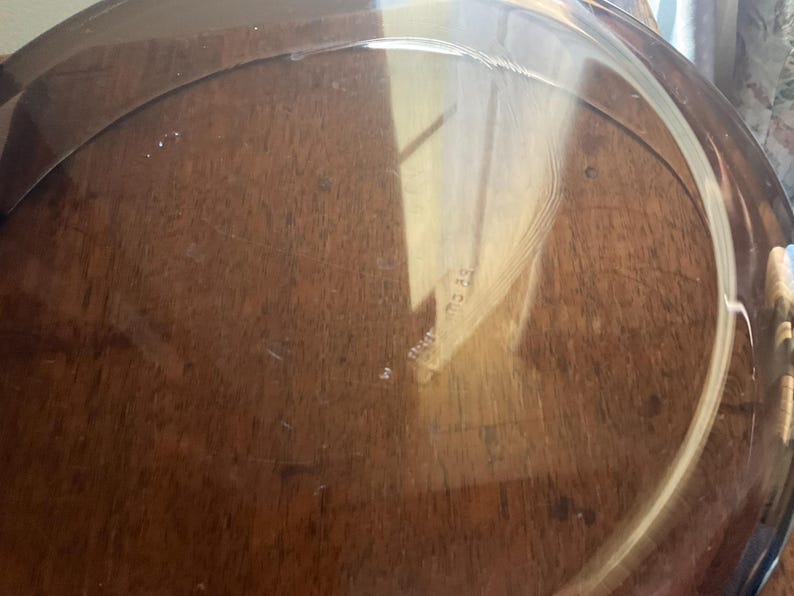 May include: A clear glass pie plate with a slightly rippled surface. The plate is sitting on a wooden surface.