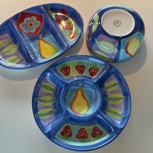 May include: A set of three blue ceramic serving dishes with fruit and floral designs. The set includes an oval divided dish, a round divided dish, and a round bowl. Each piece features a pear, strawberry, and leaf motif.