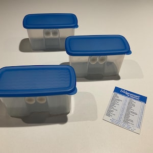 May include: Three clear plastic food storage containers with blue lids. The containers are rectangular and have small handles. A small card with the text "fridgesmart" is next to the containers.