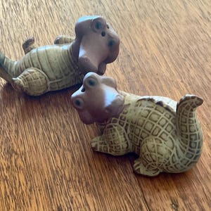 May include: A pair of ceramic salt and pepper shakers shaped like alligators. The shakers are brown and tan with a textured finish.