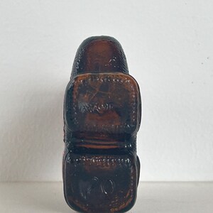 May include: A brown glass bottle stopper with a textured surface. The stopper has a square shape with rounded edges.