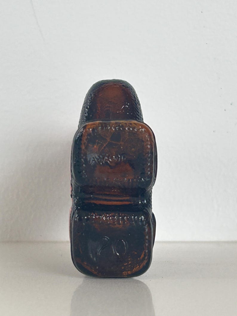 May include: A brown glass bottle stopper with a textured surface. The stopper has a square shape with rounded edges.