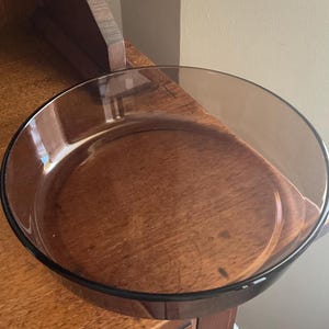 May include: A clear glass baking dish with a brown tint. The dish is round and has a slightly flared rim.