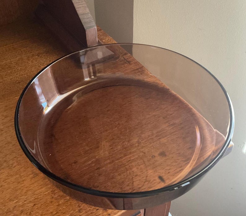 May include: A clear glass baking dish with a brown tint. The dish is round and has a slightly flared rim.