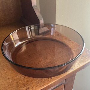 May include: A clear glass baking dish with a brown tint. The dish is round and has a slightly flared rim.