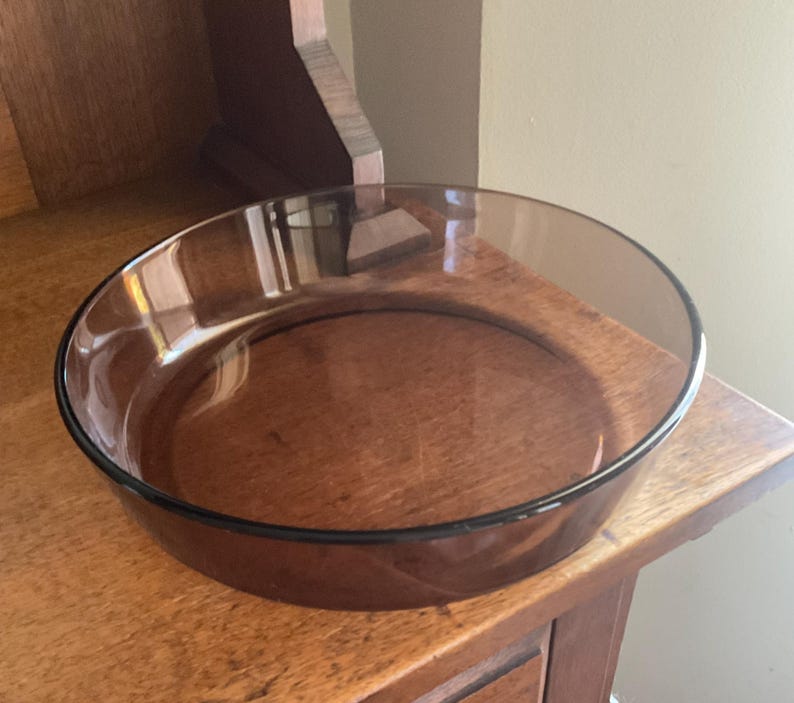 May include: A clear glass baking dish with a brown tint. The dish is round and has a slightly flared rim.