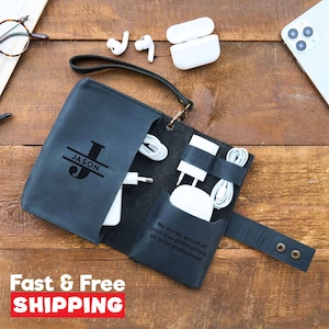 May include: A black leather tech organizer with the name "JASON" and a large initial. The organizer holds white charging cables, a phone, and a mouse. The text "We are so proud of you! Congratulations on your graduation!" is visible.