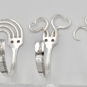 Puede incluir: Cinco pendientes de plata en forma de tenedor, cada uno con un diseño único. Los pendientes están hechos de cubiertos reciclados y presentan corazones, espirales y un diseño en forma de abanico.