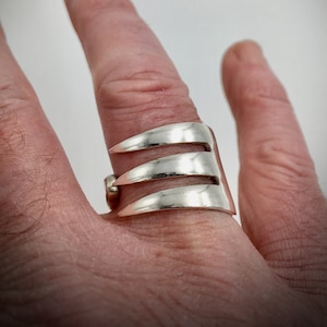 May include: A silver ring with three prongs, resembling a fork, worn on a finger.