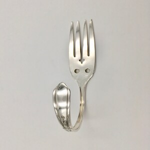 May include: A silver fork bent into a hook shape. The fork tines are intact and the handle has a decorative design.