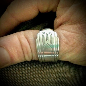 May include: A silver ring with an intricate geometric design. The ring is worn on a finger.
