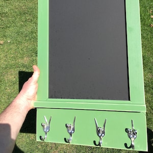 Könnte beinhalten: Eine grüne Kreidetafel mit einem Regal und drei Haken aus gebogenem Besteck. Die Haken sind in Form des 'Ich liebe dich'-Handzeichens geformt.