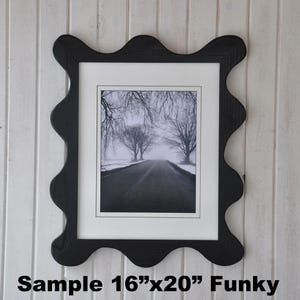 May include: Black wavy-edged picture frame with a black and white photo of a road lined with trees. The frame holds an 11x14 inch photo within a 16x20 inch frame. The frame is mounted on a white, vertically-paneled wall.