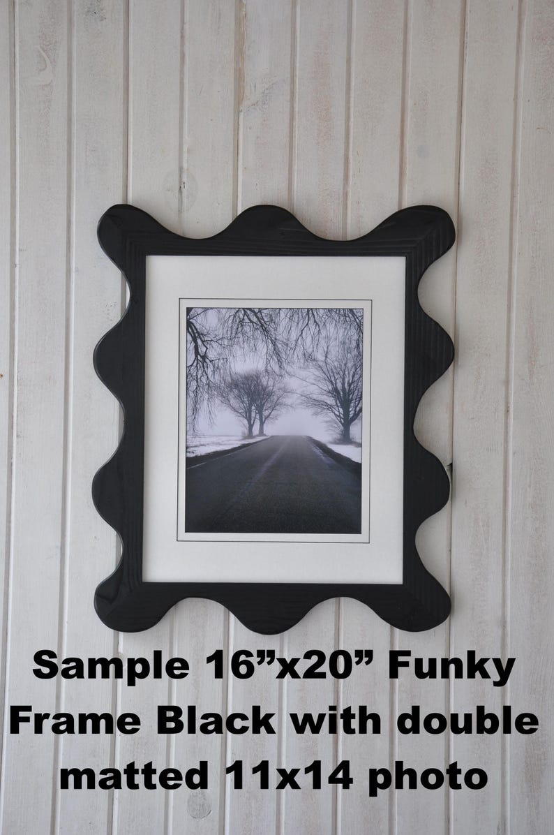 May include: Black wavy-edged picture frame with a black and white photo of a road lined with trees. The frame holds an 11x14 inch photo within a 16x20 inch frame. The frame is mounted on a white, vertically-paneled wall.