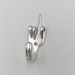 May include: A silver metal hook shaped like a middle finger, made from a recycled fork.