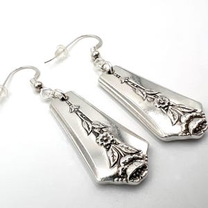 May include: A pair of silver earrings with a floral design. The earrings are made from repurposed silverware and feature a delicate rose pattern.