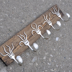 May include: A wooden coat rack with five hooks made from repurposed silverware. Each hook is shaped like an octopus tentacle with a silver finish.