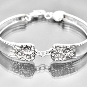 May include: A silver bracelet made from a repurposed spoon with a floral design. The bracelet is open and has a chain clasp.
