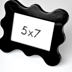 K&ouml;nnte beinhalten: Schwarzer, wellenf&ouml;rmiger Bilderrahmen mit einem wei&szlig;en Passepartout und dem aufgedruckten Text "5x7".