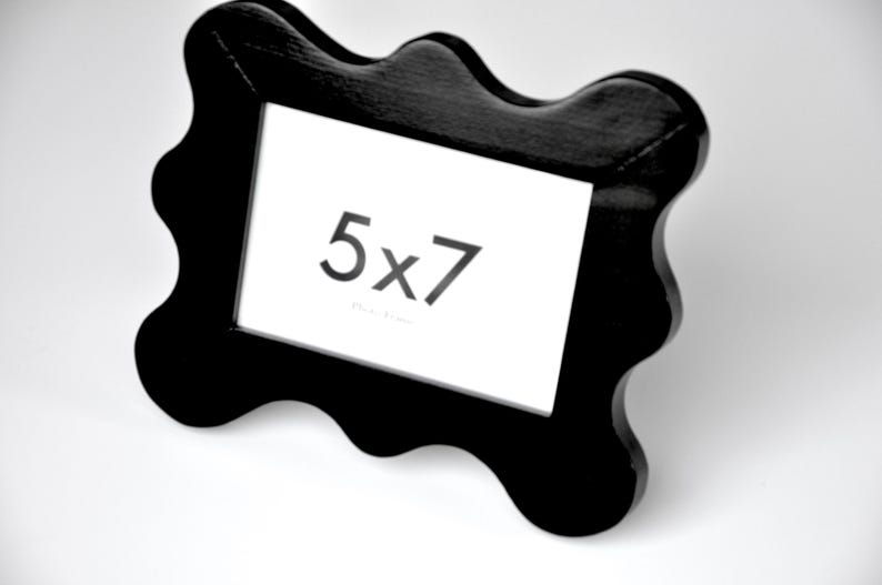 K&ouml;nnte beinhalten: Schwarzer, wellenf&ouml;rmiger Bilderrahmen mit einem wei&szlig;en Passepartout und dem aufgedruckten Text "5x7".