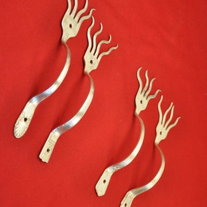 Peut inclure: Quatre crochets en métal argenté en forme de main à cinq doigts. Les crochets sont pliés en forme de courbe et sont disposés en rangée sur un fond rouge.