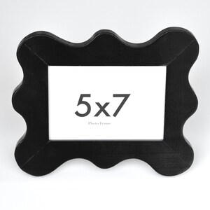 K&ouml;nnte beinhalten: Schwarzer, wellenf&ouml;rmiger Bilderrahmen mit einer &Ouml;ffnung von 12,7 x 17,8 cm. Der Rahmen ist aus Holz und hat eine glatte Oberfl&auml;che.
