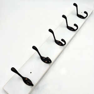 May include: White wooden coat rack with five black metal hooks. The rack is distressed and has a rustic look.