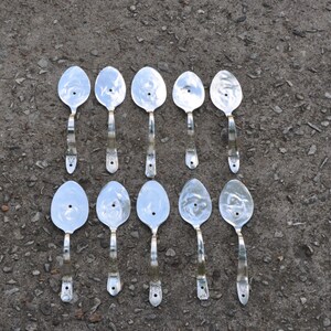 May include: Twelve silver spoons with holes in the bowl, arranged in two rows of six. The spoons have a gold-colored handle.