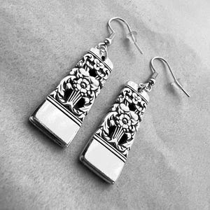 Puede incluir: Un par de pendientes colgantes de plata con un diseño floral. Los pendientes están hechos de cubiertos reciclados.