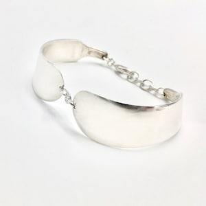 May include: A silver bracelet with two curved, flat pieces connected by a chain.