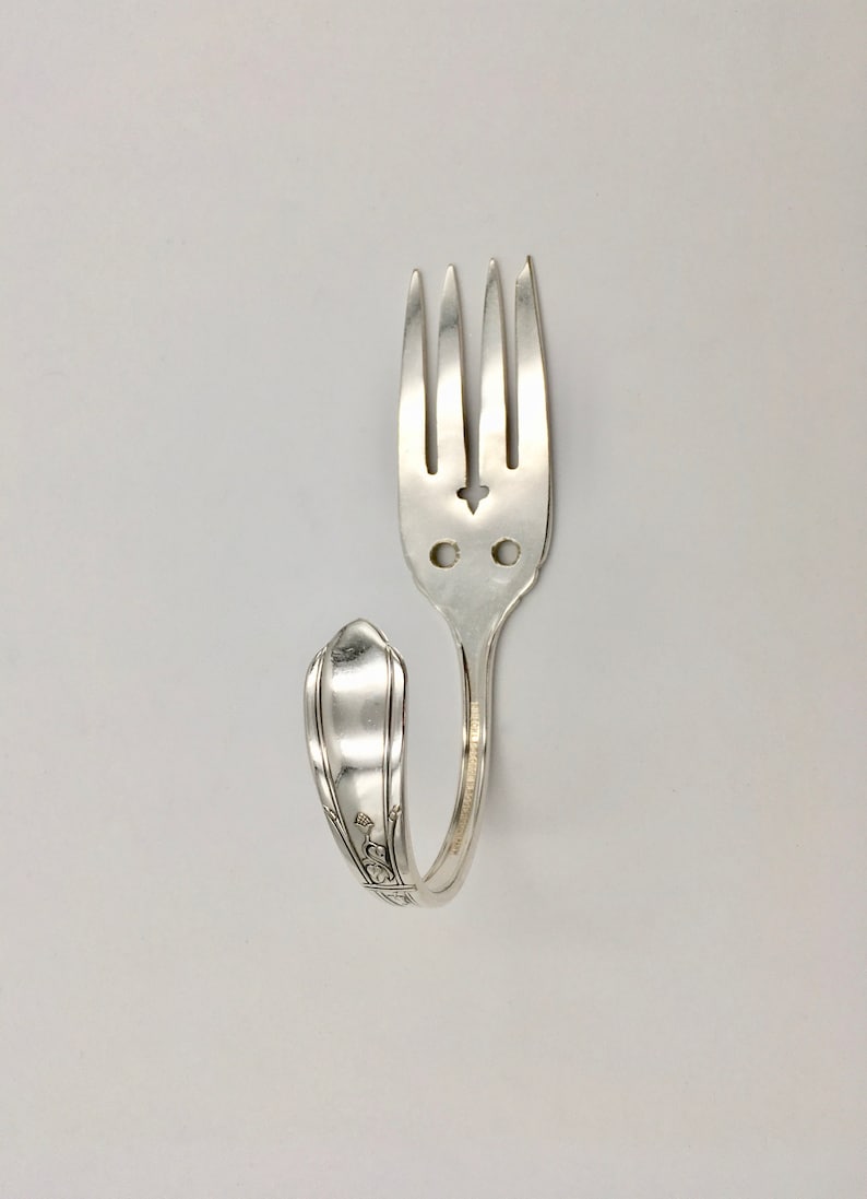 May include: A silver fork bent into a hook shape. The fork tines are intact and the handle has a decorative design.