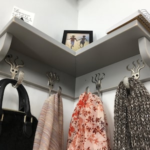 May include: A gray corner shelf with three hooks on each side. The hooks are decorated with a silver octopus design. A black purse hangs on one hook, and three scarves hang on the other hooks. A small framed photo sits on the shelf, and a notebook is on the top of the shelf.