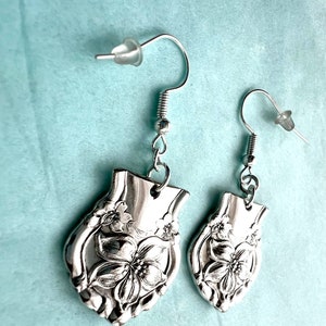 May include: A pair of silver earrings with a floral design. The earrings are made from repurposed silverware and feature a delicate floral pattern.