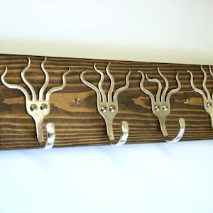 May include: A wooden wall-mounted coat rack with four hooks made from repurposed silverware. The hooks are shaped like an octopus with a silver finish.