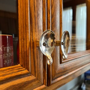 Könnte beinhalten: Nahaufnahme einer Holztür eines Schranks mit zwei Löffelgriffen. Die Löffel sind silbern und wurden mit einer Metallstange an der Tür befestigt. Die Schranktür ist aus dunklem Holz mit einer Maserung.