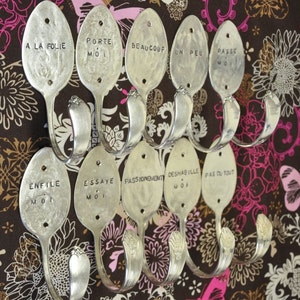 Peut inclure: Neuf cuillères en argent transformées en crochets avec des phrases françaises gravées dessus, notamment "A la folie", "Porte moi", "Beaucoup", "Un peu", "Passe moi", "Enfile moi", "Essaye moi", "Passionnement", "Deshabille moi", et "Pas du tout".