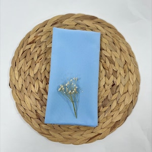 May include: A light blue napkin with a small bouquet of white flowers on top of a woven round placemat.