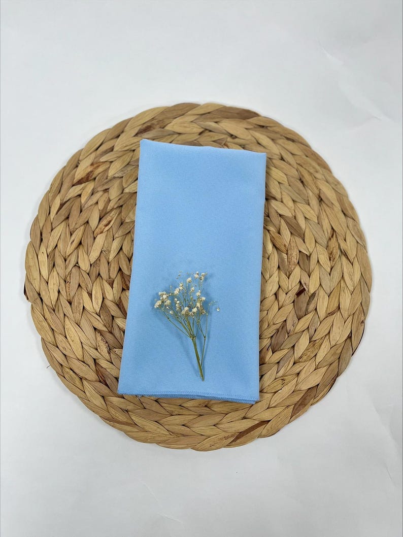 May include: A light blue napkin with a small bouquet of white flowers on top of a woven round placemat.