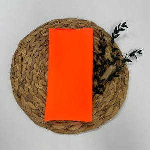 May include: A bright orange fabric swatch on a woven straw mat.