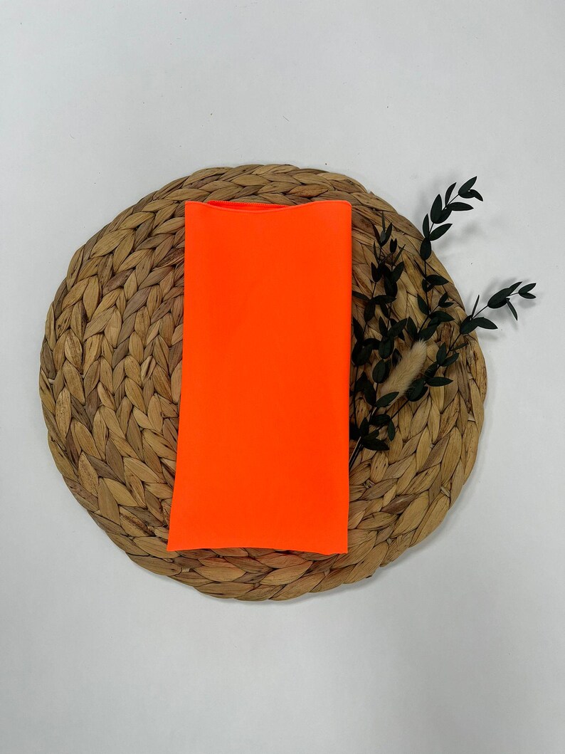 May include: A bright orange fabric swatch on a woven straw mat.